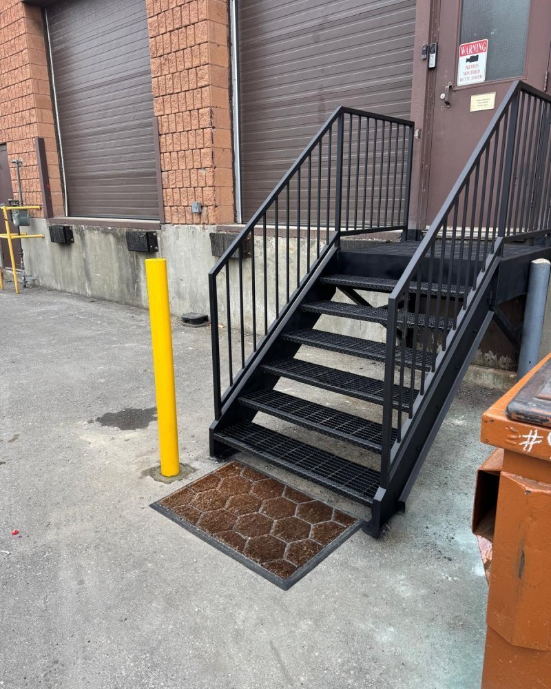 Steel egress staircase installed inside an Ontario warehouse — switchback flights with intermediate landing and 42-inch guards